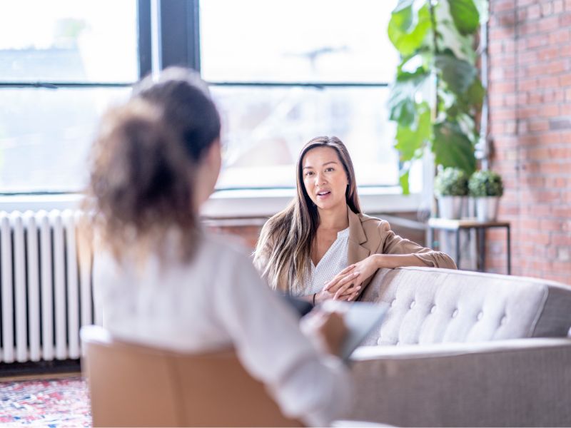 Woman talking with a therapist during a one-on-one counseling session in a bright, comfortable office. Image representing interpersonal therapy (IPT), focused on relationships, communication skills, and improving mood and mental health.