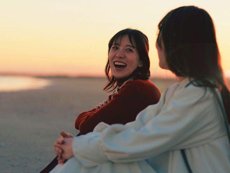 Two women sitting together outdoors at sunset, smiling and talking, showing connection and support. Image representing a mental health Intensive Outpatient Program (IOP), emphasizing community, therapy, and recovery while living at home.