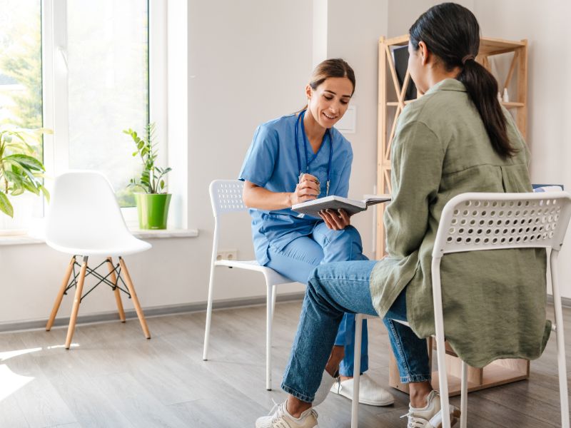 Mental health clinician meeting with a client in a bright, calm room, taking notes during a supportive conversation. Image representing residential mental health treatment, inpatient stabilization, and personalized therapy in a structured setting.